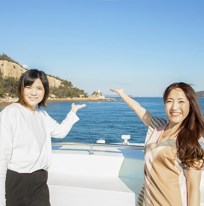 停泊したクルーズ船のフライングデッキから、京の上臈島の白い灯台を紹介する二人の女性