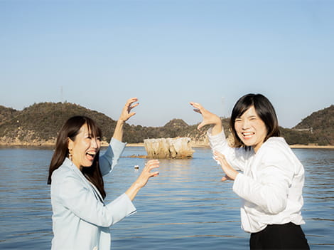海にある巨大な石を登っているようなポーズをとっている二人組の女性