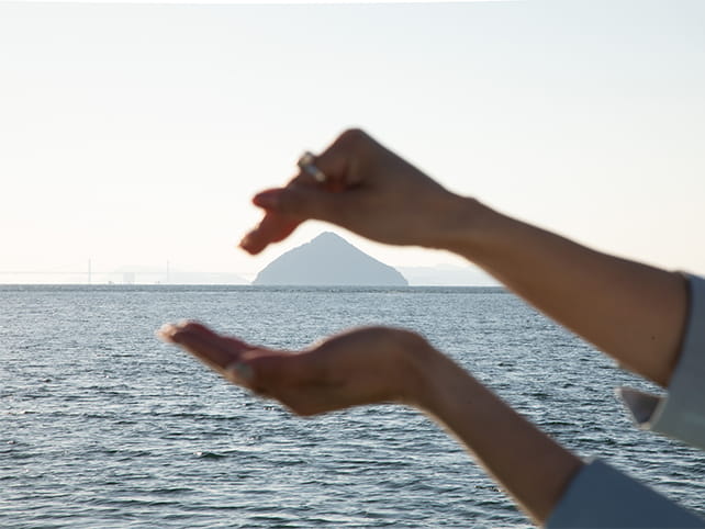 おにぎりの形に見える大槌島を、手で握るように撮影している女性の手