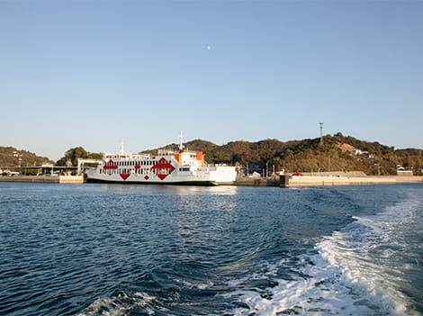 白波を立てながら航行するクルーズ船後方デッキから見た、直島の宮浦港と定期フェリー